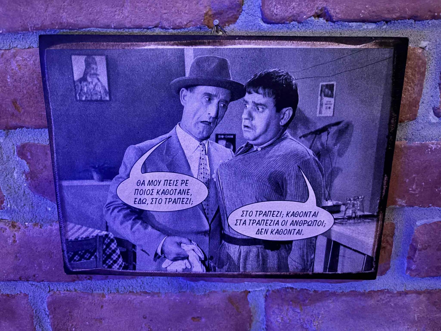 Framed still from a Greek film with a line about the table, on a brick wall at Karnagio